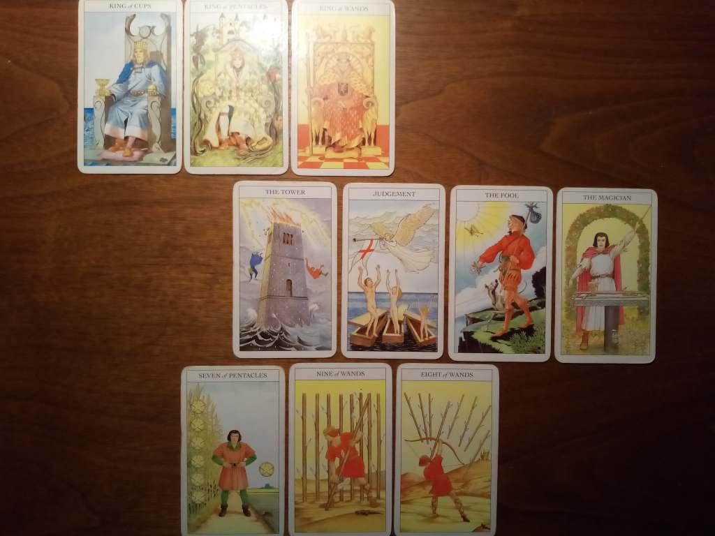 Tarot cards laid out on a table: King of Cups, King of Pentacles, King of Wands, the Tower, Judgement, the Fool, the Magician, Seven of Pentacles, Nine of Wands, Eight of Wands