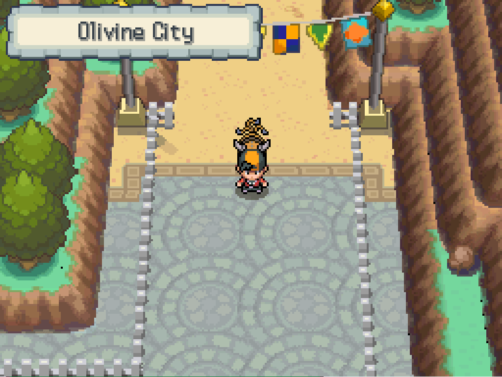 Entering Olivine City: cliffs on either side, streets paved with an elegant circular pattern, white fences, a line of pennants overhead.